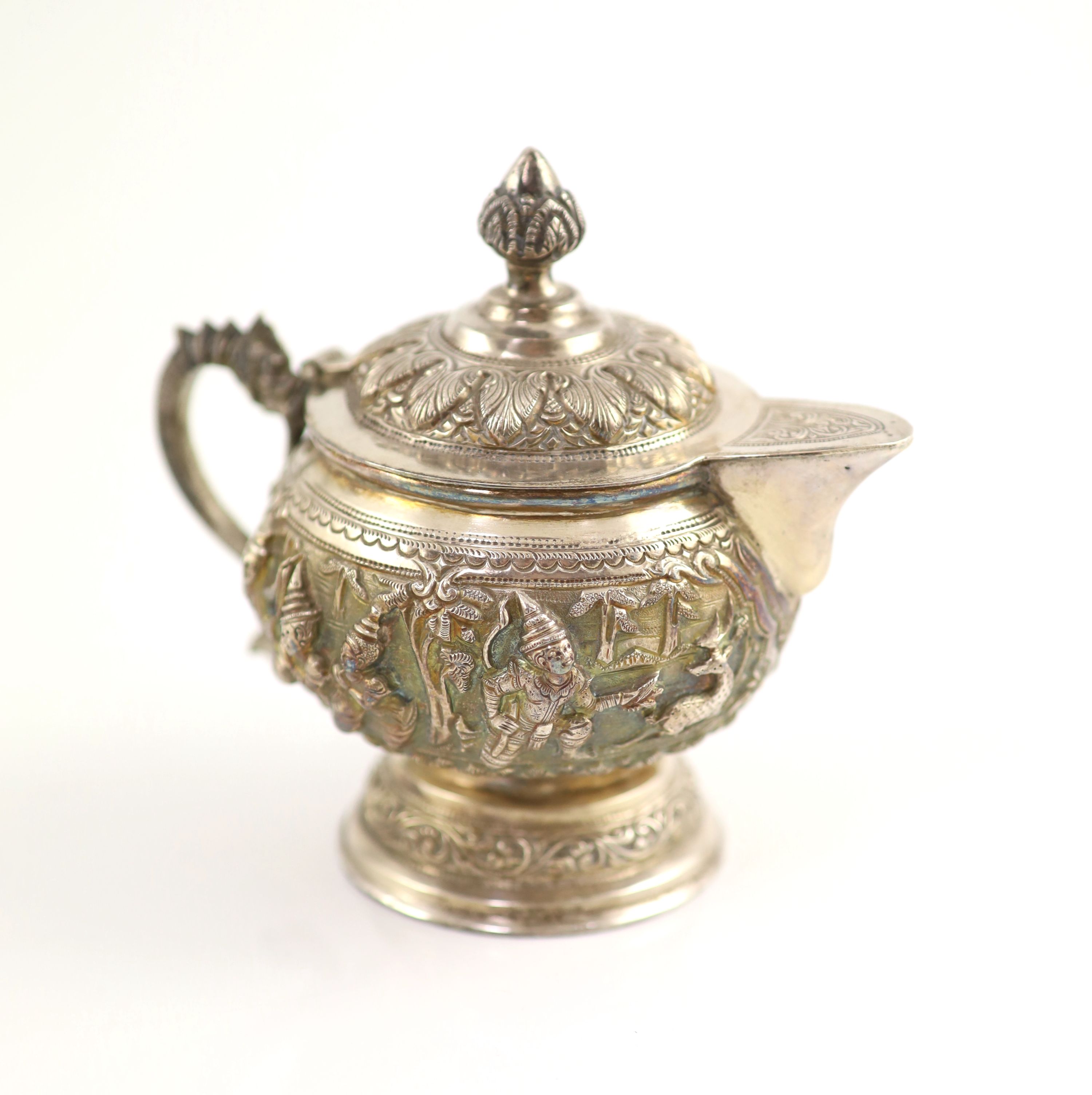 An impressive Burmese Sterling silver (950) three-piece tea service, with tray, cast with figures, teapot with cockerel spout and figural handle